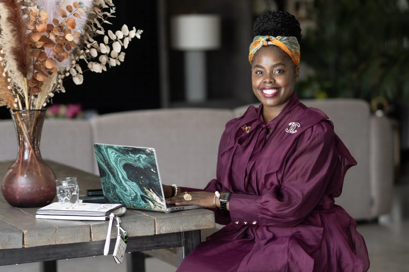 Ngoni Diana Johns working on a laptop at a wooden table beside a vase of dried flowers
